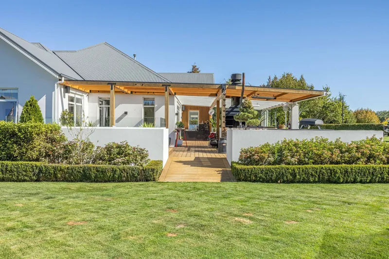 Home exterior with timber pergola, outdoor living area and manicured hedges